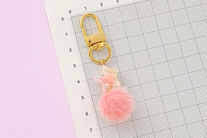Pink fur ball star keychain with golden clasp measured on a scale showing size details