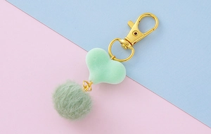 Dettaglio portachiavi con pompon verde chiaro e ciondolo a cuore con gancio dorato
