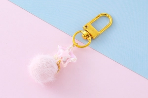 Detail of candy-colored pink plush pom pom and clear star keychain with golden D-ring clasp