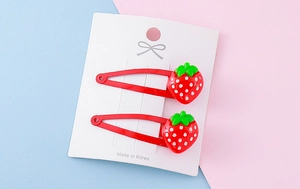 Detail view of two red strawberry hair clips with white dots on a display card