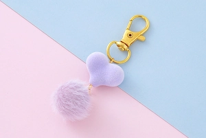 Dettaglio di ciondolo a cuore viola e pompon peloso con chiusura in metallo dorato
