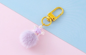 Detail of candy color star pendant and soft purple faux fur pompom on gold keychain
