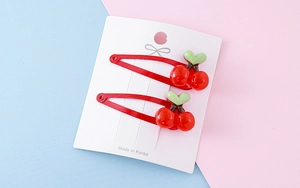 Detail view of two red cherry hair clips on a white display card with green leaves