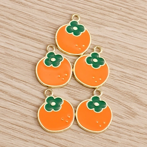 Detailed view of 5 orange persimmon pendants with gold metal edges on a light wood background