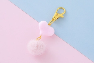 Dettaglio di ciondolo a cuore rosa e pompon di pelliccia con chiusura dorata