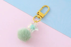 Macro view of pastel green pom pom and iridescent star pendant with golden lobster clasp