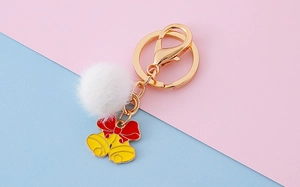 Détail d'un porte-clés pompon blanc avec un pendentif clochette en émail rouge et jaune