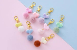 Dettaglio di portachiavi a cuore in peluche con pompon e moschettoni dorati