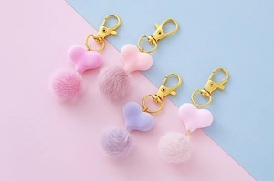 Dettaglio di quattro portachiavi a pompon a cuore in colori pastello con ganci oro