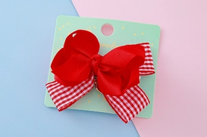 Détail d'une pince à cheveux avec nœud rouge superposé et motif à carreaux chic