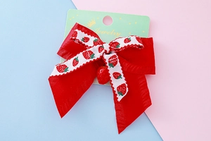 Détail d'une barrette à cheveux nœud rouge avec breloque fraise sur carte