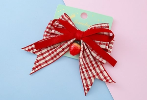 Détail d'une pince à cheveux avec nœud en velours rouge, carreaux et breloque fraise