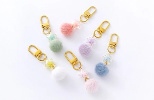 Close-up of fluffy pastel pom-pom keychains with golden star charms in six macro colors