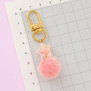 Pink star pom pom keychain with gold clasp and star charm on measuring grid background