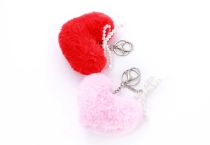Detail of red and pink plush heart keychains with faux pearl bows on white background