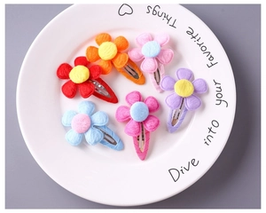 Close-up of six colorful fabric flower hair clips with soft texture in a white ceramic dish