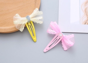 Detail of pink and yellow embroidered lace mesh bow hair clips on a wooden tray