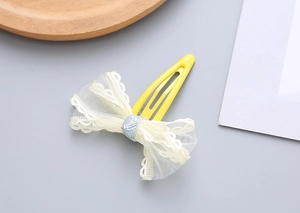 Detailed close-up of a sweet beige lace mesh bow on a yellow metal BB hair clip