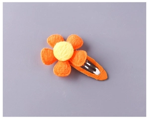 Detail showing orange plush five-petal flower hair clip with fabric-wrapped metal base