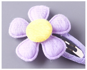 Detailed macro shot of a purple felt flower hair clip with a soft yellow pompom center