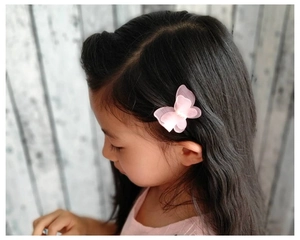 Détail d'une pince à cheveux papillon en maille rose avec perle sur une fille