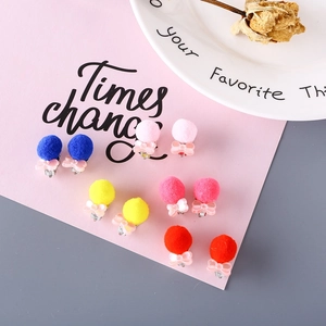 Colorful pom-pom bow clip-on earrings for kids with metal clips on pink background