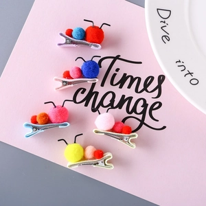 Close-up of five colorful plush pom-pom hair clips for kids on pink card background