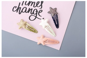 Close-up of four glittery star-shaped hair clips in gold, pink, white, and navy blue