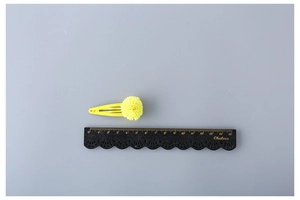 Close-up of yellow pom-pom hair clip on a painted metal BB clip measured with a ruler