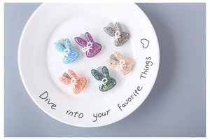 Detailed view of six colorful glitter bunny hair clips with lace bows on a white plate