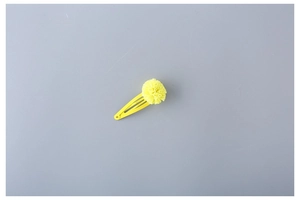 Detail view of a yellow fluffy tulle pom pom hair clip with matching lacquered metal base