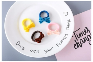 Detailed view of four colorful velvet bow hair ties displayed on a white porcelain plate