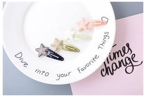 Detailed view of four glitter star hair clips in pink, cream, gold and navy blue