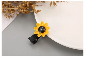 Detail of sunflower hair clip with yellow petals and polka dot center on a white plate