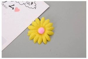 Detail view of yellow sunflower hair clip with pink fuzzy center and black metal fastener