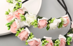 Dettaglio di un cerchietto floreale con rose finte rosa e bianche e foglie verdi