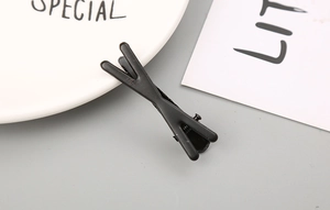 Détail d'une pince à cheveux noire mate en forme de X avec une finition givrée sur fond neutre