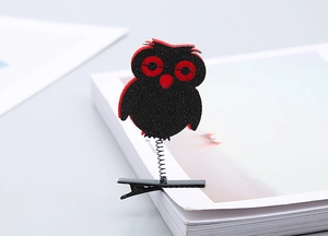Detail of glitter owl spring clip made of red felt on white book page edge