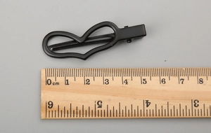 Détail d'une pince à cheveux de 5 cm en métal noir en forme de cœur sur une règle graduée