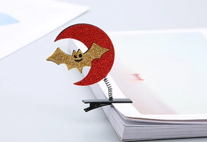 Detail of Halloween sequin hair clip with glitter moon, bat and spring on a white book