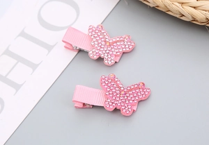 Détail de deux pinces à cheveux papillon en strass rose avec ruban gros-grain doux