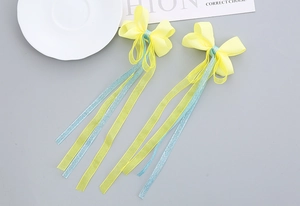 Détail de barrettes noeud jaunes avec de longs rubans fluides et accents scintillants