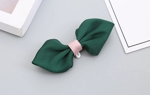 Detailed close-up of dark green handmade bow tie with pink ribbon center on grey background