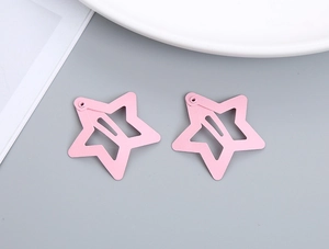 Detail view of two light pink star-shaped metal hair clips on a minimalist background