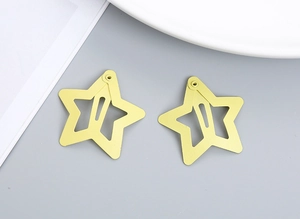 Close-up of two matte yellow hollow star-shaped metal snap hair clips on a desk