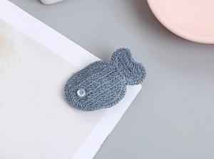Detalle de una pinza para el pelo de pez hecha a mano con tejido de punto gris y ojo de cristal