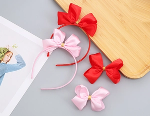 Dettaglio di set cerchietto e clip con fiocchi in raso rosso e rosa per bambina su legno