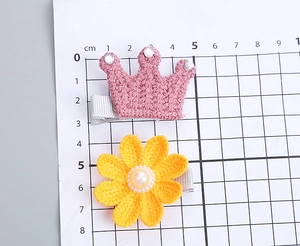 Detalle de pinzas de pelo de ganchillo con corona y girasol sobre fondo de escala