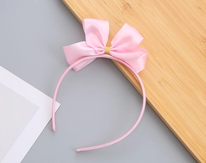 Dettaglio di un cerchietto in raso rosa con fiocco, centro dorato e trama in seta fine
