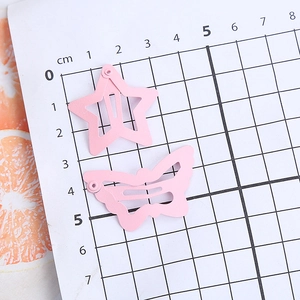 Pink metal butterfly and star hair clips for girls displayed on a metric scale grid